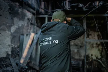 Technik kryminalistyki fotografuje zniszczenia po pożarze wewnątrz spalonego budynku.