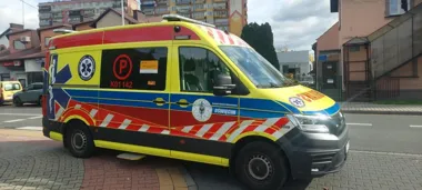 Karetka pogotowia ratunkowego z Oświęcimia stoi na brukowanym chodniku przy ulicy w zabudowie miejskiej.