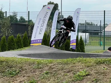 Kolarz w czarnym stroju i kasku pokonuje górkę na torze pumptrack podczas zawodów na Małopolskiej Arenie Mistrzostw.